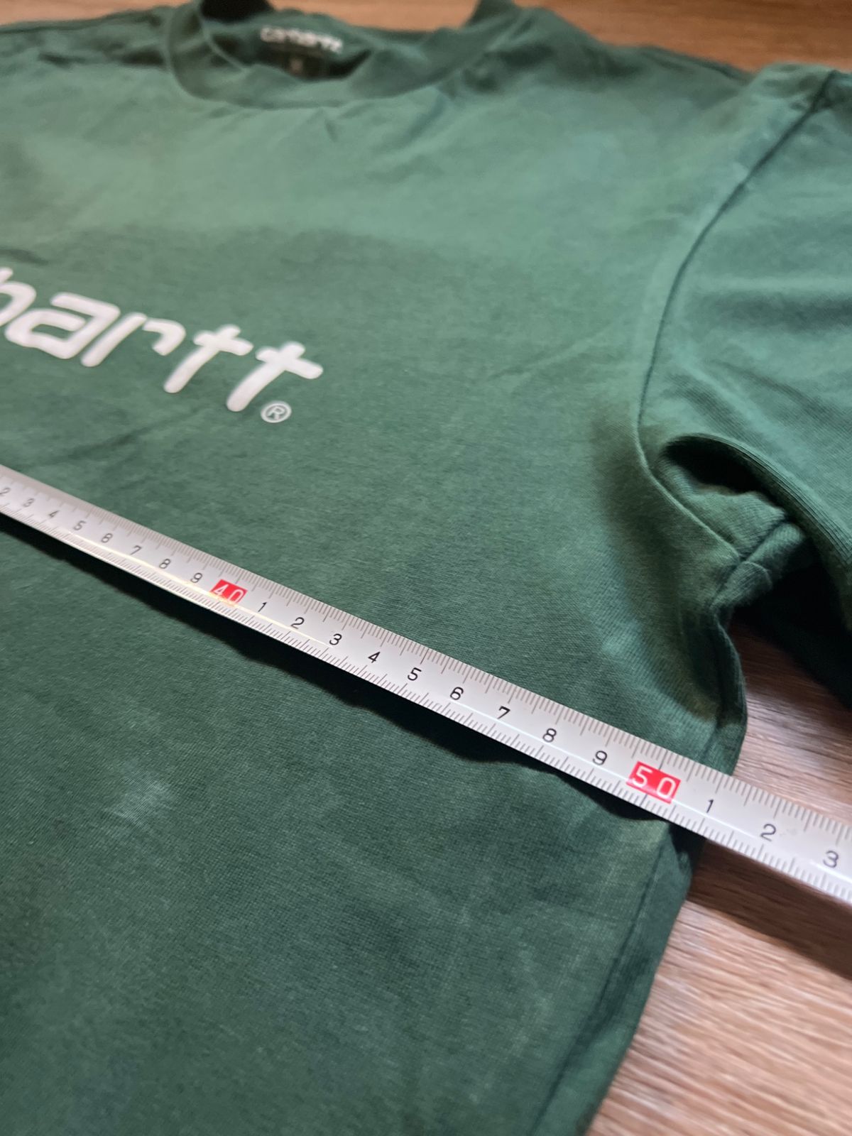 Una cinta métrica midiendo el ancho de la camiseta verde Carhartt
